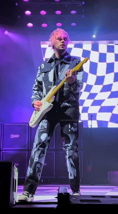 a man with pink hair holding a guitar on stage