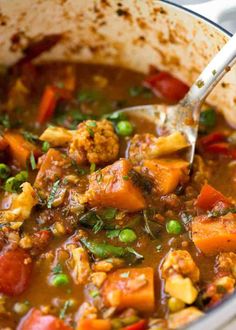 a pot filled with stew and vegetables on top of a table next to a spoon