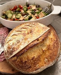 a loaf of bread sitting on top of a cutting board next to a bowl of salad