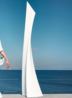 a woman standing next to a tall white sculpture near the ocean on a sunny day