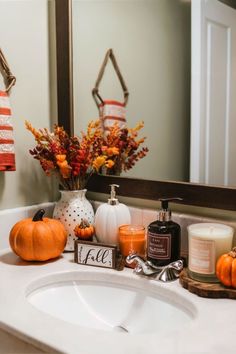 a white sink sitting under a mirror next to a candle and some pumpkins on top of it