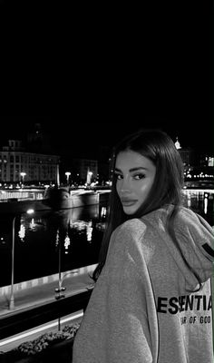 black and white photo of woman in hoodie looking at camera with city lights behind her