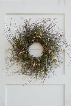 a white door with a wreath hanging on it's side and flowers in the middle