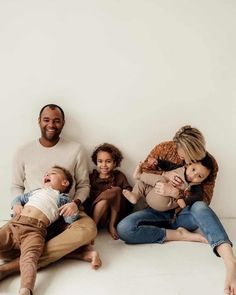 a group of people sitting on the ground with one holding a baby and smiling at the camera