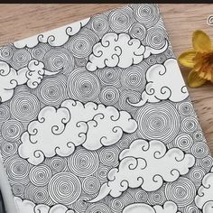 a drawing book with an image of clouds and flowers on the table next to it