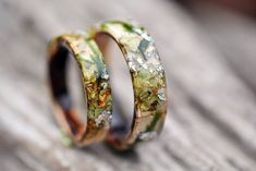 two wedding rings with green and yellow flowers on them sitting on a piece of wood