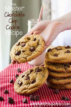 chocolate chip cookies and milk being held by a woman's hand over a red checkered tablecloth