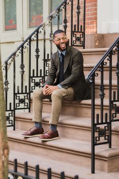 a man sitting on the steps of a building wearing a suit and tie, smiling at the camera