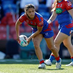 a woman holding a rugby ball in her right hand and looking down at the ground