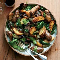 a bowl filled with meat and vegetables on top of a wooden table next to a glass of wine