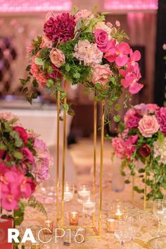 tall gold vases filled with pink flowers and greenery on top of a table