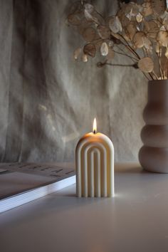 a white candle sitting on top of a table next to a book