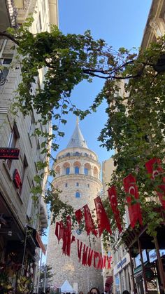 people are walking down the street in front of a tall building with flags hanging from it's sides