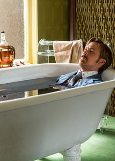 a man laying in a bathtub next to a bottle of whiskey on the floor