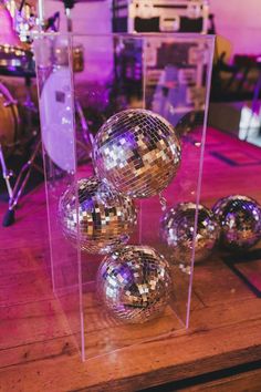 shiny disco balls in a clear case on a wooden table with purple lighting behind them