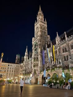 a person walking in front of a tall building at night with lots of flags hanging from it's sides