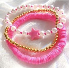 two bracelets with beads and a pink star on them are laying on a white cloth