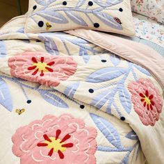 a bed with pink and blue flowers on the comforter, pillows and pillow cases