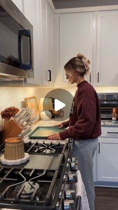 a woman standing in front of an oven preparing food on the stove top with a wooden spatula