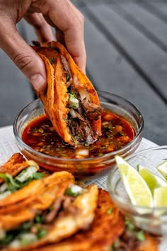 a person dipping some food into a bowl with sauce and limes on the side