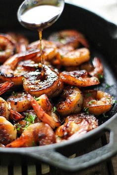 the shrimp is being drizzled with sauce from a spoon in a skillet