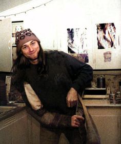 a man with long hair standing in a kitchen