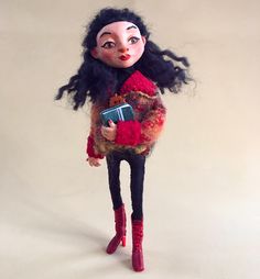 a doll with black hair and red boots holding a blue box in her hands, on a white background