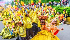 people in yellow dresses and hats are dancing on the street with their hands up to the sky