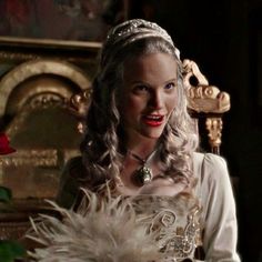 a woman wearing a tiara with feathers on her head sitting in front of a chair