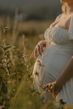 a pregnant woman standing in a field with her hand on her belly