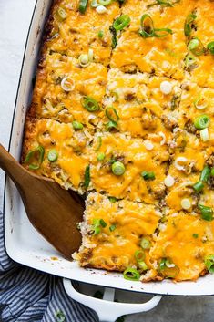 a casserole dish with green onions, cheese and meat in it next to a wooden spoon