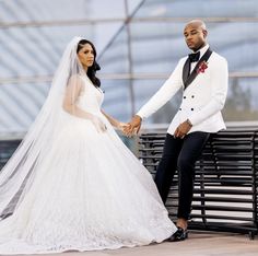 a bride and groom sitting on a bench in front of a glass building holding hands