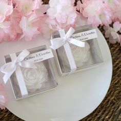 two small boxes with white frosted roses in them on a plate next to pink flowers