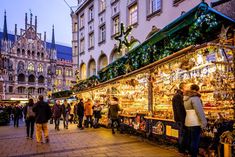 many people are walking around an outdoor market with christmas decorations and lights on the buildings