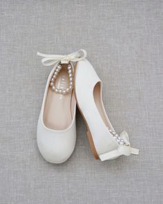 two pairs of white shoes with pearls tied to the toe and heels are on top of each other