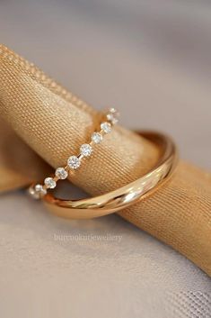 two wedding rings sitting on top of each other next to a gold napkin and cloth