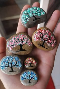 four rocks with trees painted on them are in the palm of someone's hand