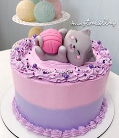 a pink and purple cake with a cat laying on it's back in the middle