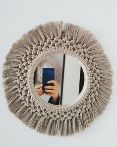 a person holding a cell phone in front of a round mirror with fringes on it