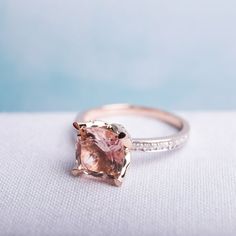 a pink diamond ring sitting on top of a white cloth covered table next to a light blue background