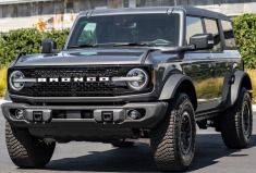 the front end of a black jeep parked in a parking lot next to some bushes