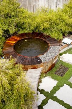 an outdoor hot tub in the middle of a garden with grass and rocks around it