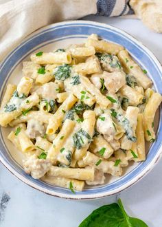 a blue and white bowl filled with pasta covered in chicken, spinach and cheese