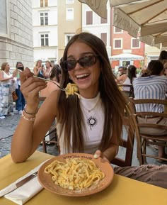 a woman sitting at an outdoor table eating pasta