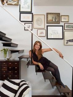 a woman sitting on top of a stair case next to a wall filled with pictures