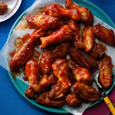 a plate full of chicken wings with sauce on the side and a fork next to it