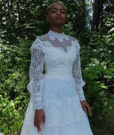 a woman wearing a white dress standing in front of trees