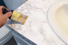 a person using a brush to paint a marble counter top with white and gold accents