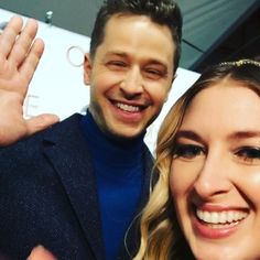 a man standing next to a woman with her hand up and smiling at the camera