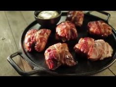 meat wrapped in bacon on a black plate with dipping sauces and green dipper